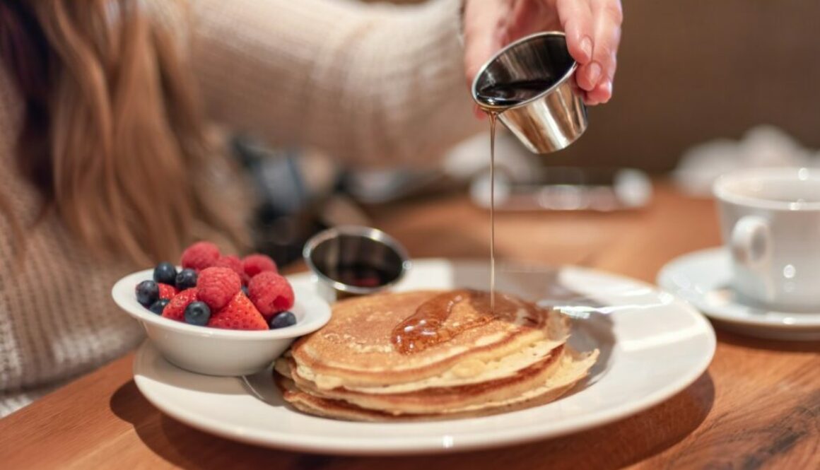 meeting-friends-for-breakfast-young-woman-pouring-warm-maple-syrup-on-pancakes_t20_pR7238